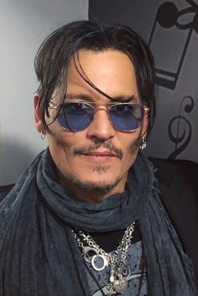 Johnny Depp mit blauer Sonnenbrille und Schal. Einzelne Haarsträhnen fallen ihm ins Gesicht.