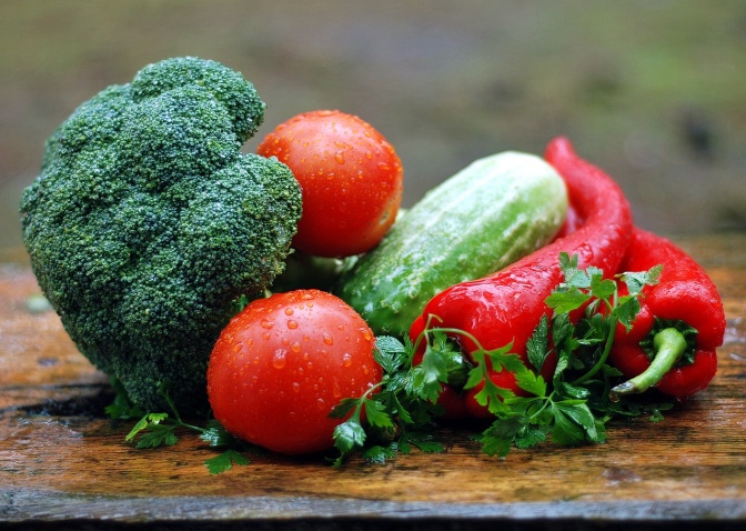 Verschiedene Gemüse auf einem Holzbrett: Ein Brokkoli, eine Gurke, mehrere Tomaten, rote Spitzpaprika und glatte Petersilie