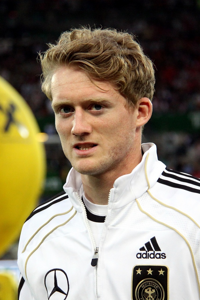 André Schürrle in einer weißen Trainingsjacke mit 3 schwarzen Streifen und verschiedenen Sponsoren-Logos