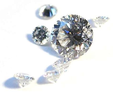 7 geschliffene Diamanten in verschiedenen Größen liegen nebeneinander und werfen Schatten auf den Untergrund.