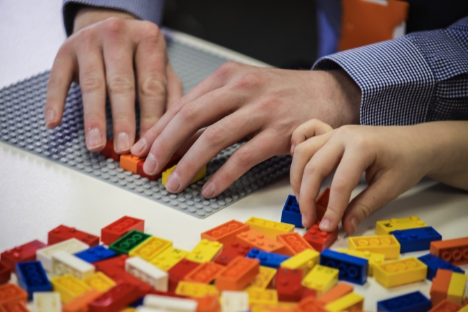 Eine Person ertastet die Legosteine mit Braille-Schrift mit beiden Händen. Daneben liegt ein Haufen mit vielen weiteren Legosteinen.