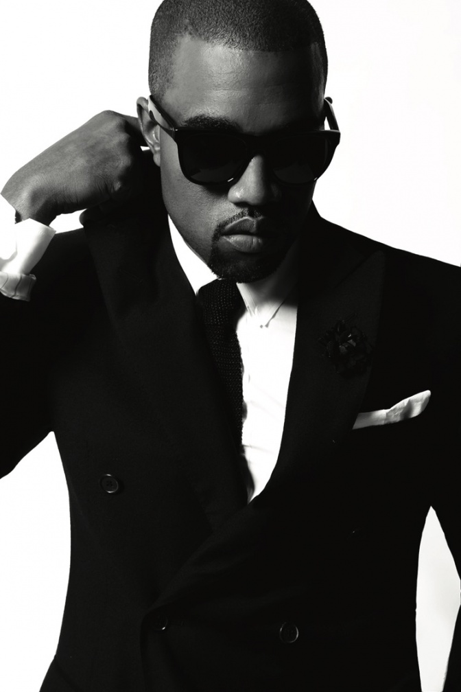 Ein schwarz-weiß-Foto von Kanye West in Anzug und Krawatte mit schwarzer Sonnenbrille.