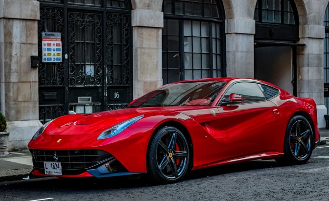Ein glänzender, roter Ferrari ist an der Straße geparkt, vor einem Gebäude mit Säulen.