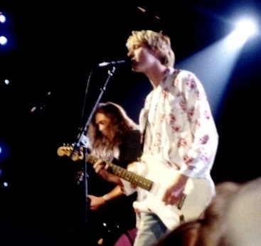 2 Musiker auf der Bühne. Kurt Cobain singt in ein Standmikro und spielt Gitarre, hinter ihm ist Krist Novoselic zu sehen.