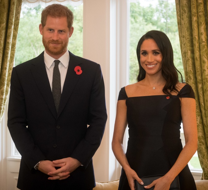 Prinz Harry und Herzogin Meghan stehen in festlicher Kleidung nebeneinander. Beide haben die Hände im Schoß ineinander verschränkt.