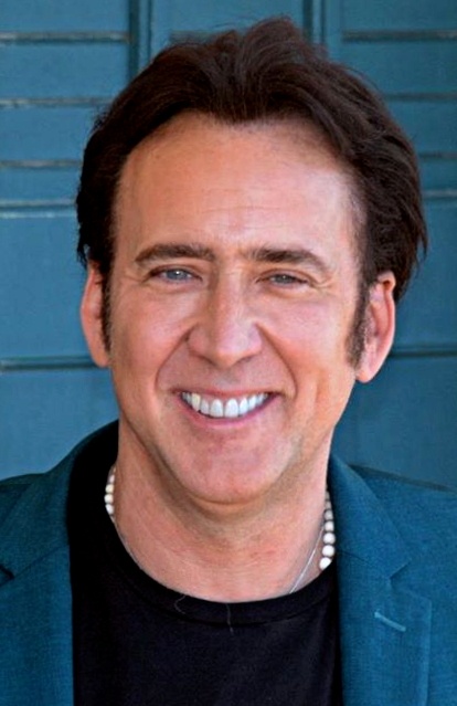 Nicolas Cage in T-Shirt und Sakko. Er hat kurze braune Haare und lächelt.