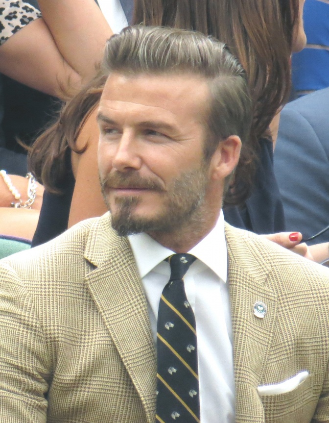 David Beckham in Anzug und Krawatte mit nach hinten frisierten Haaren und Bart.