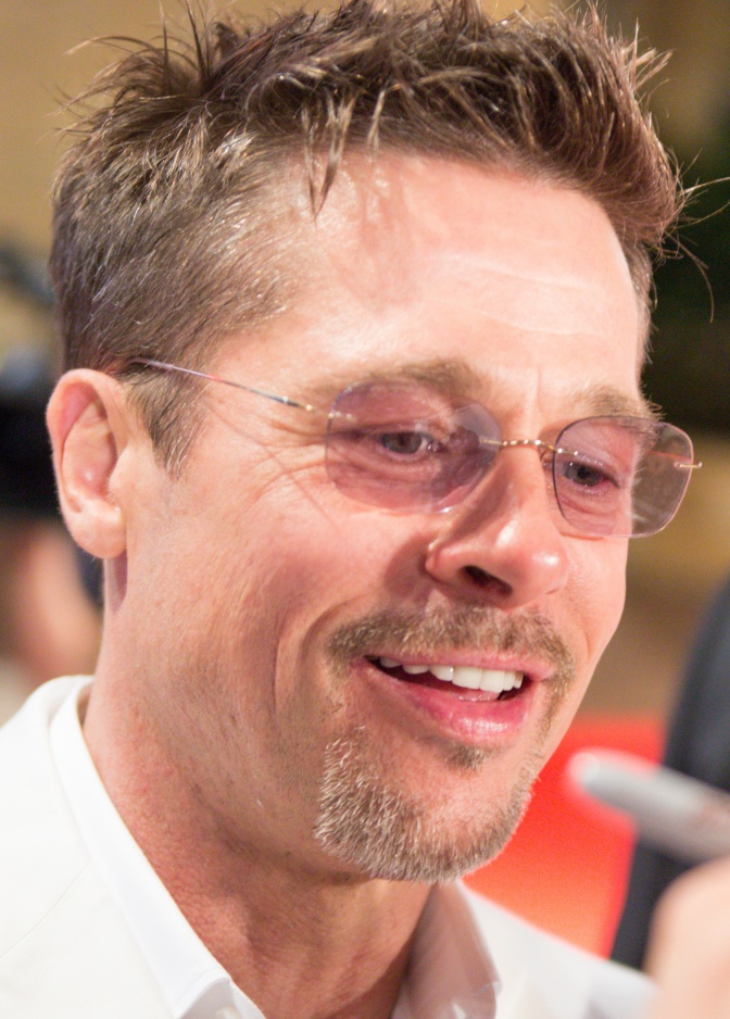 Brad Pitt mit Dreitagebart und Brille. Er trägt ein Hemd und hat kurze braune Haare.