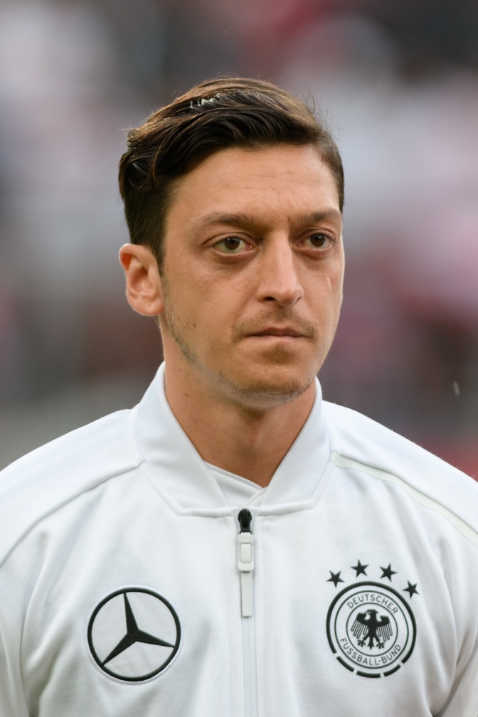 Mesut Özil in einer weißen Trainingsjacke mit Sponsorenlogos unter anderem Mercedes.