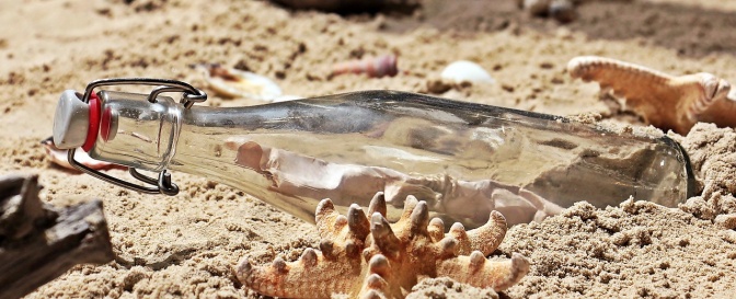 Eine Flasche mit Bügelverschluss liegt im Sand. Im Inneren sieht man ein zusammengerolltes Stück Papier.