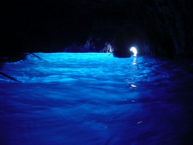 Leuchtend blaues Wasser in der Blauen Grotte, darauf rudert ein Ruderboot.