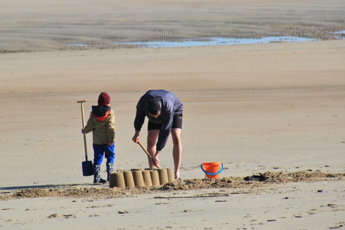 Ein Erwachsener und ein Kind spielen im Sand und bauen eine Sandburg.