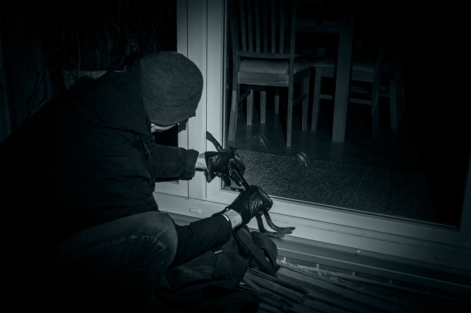 Ein Mann in dunkler Kleidung bricht mit einem Stemmeisen eine Tür auf.