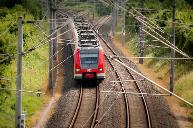 Ein Zug mit der Aufschrift DB fährt über Gleise durchs Grüne.