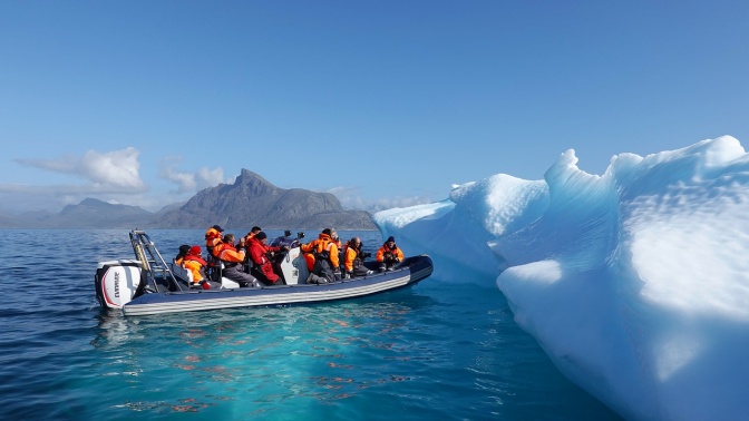 Eine Gruppe von Menschen paddelt in einem Schlauchbott an Eisschollen heran.