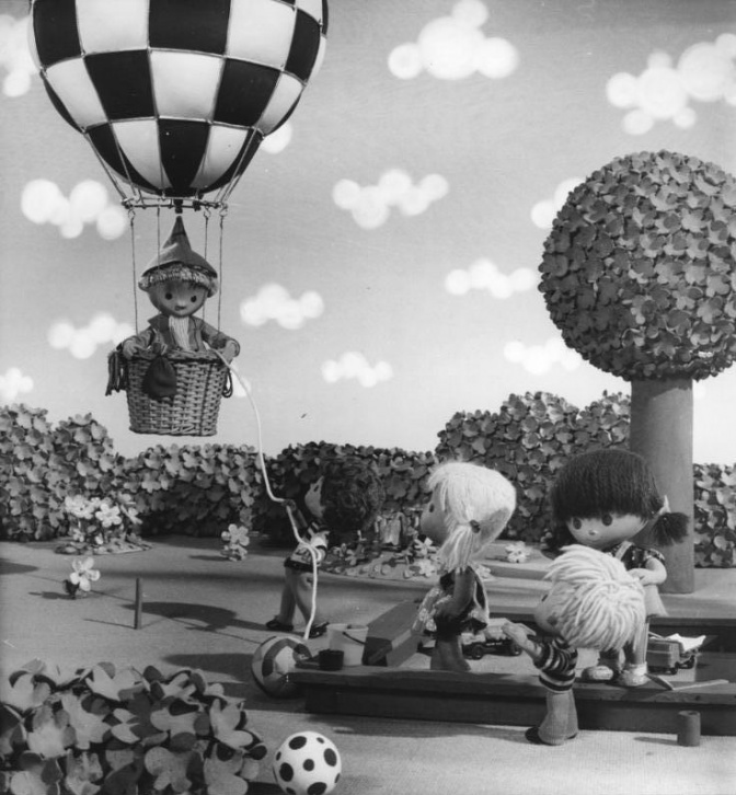 Das Sandmännchen fliegt in einem Heißluftballon auf 2 Kinder zu. Es sind Puppen in einer gebastelten Parklandschaft.