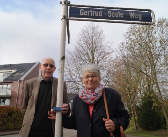 Zwei ältere Personen mit Brille fühlen das Straßenschild des Getrud-Seele-Wegs.