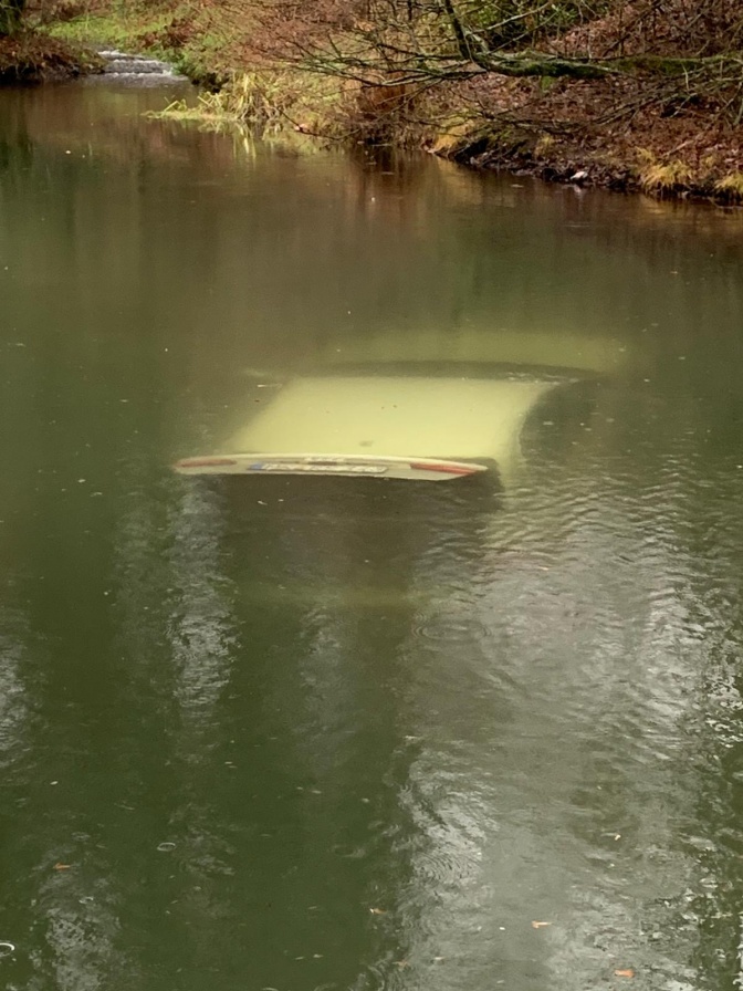 Ein hellgrünes Auto mit geöffnetem Kofferraum treibt kurz unterhalb der Wasseroberfläche eines Teiches