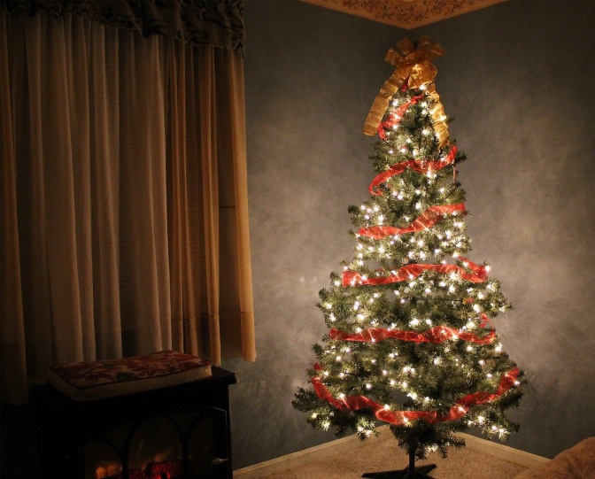 Ein festlich beleuchteter und geschmückter Weihnachtsbaum. An der Spitze prangt eine große, goldene Schleife.