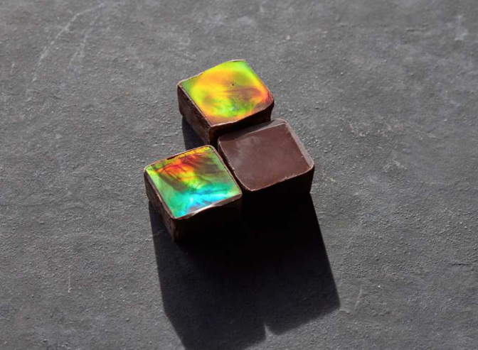 Drei quadratische Schokoladenpralinen, die in Regenbogenfarben schimmern