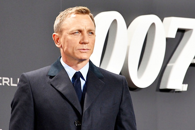 Daniel Craig in Anzug und Krawatte vor einer Wand mit einem großen 007-Logo.