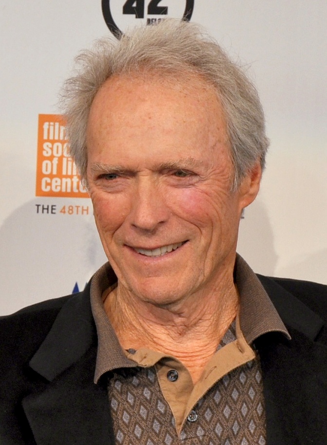 Clint Eastwood in einem gemusterten Hemd und Sakko mit dünnem Haar vor einer Logowand