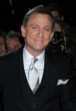 Daniel Craig mit blonden Haaren in Anzug und Krawatte. Er lächelt in die Kamera.