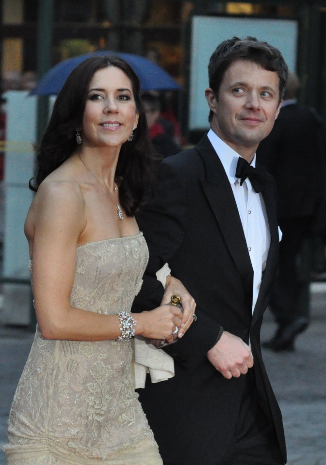 Kron-Prinz Frederik und Kron-Prinzessin Mary in festlicher Kleidung. Er trägt Anzug und Fliege, sie ein schulterfreies Abendkleid. Beide haben sich beieinander untergehakt.