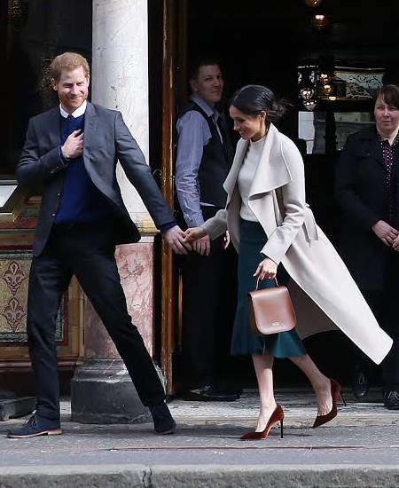 Prinz Harry und Herzogin Meghan, er trägt Anzug und Krawatte, sie Mantel und Pumps. Sie halten sich an den Händen.