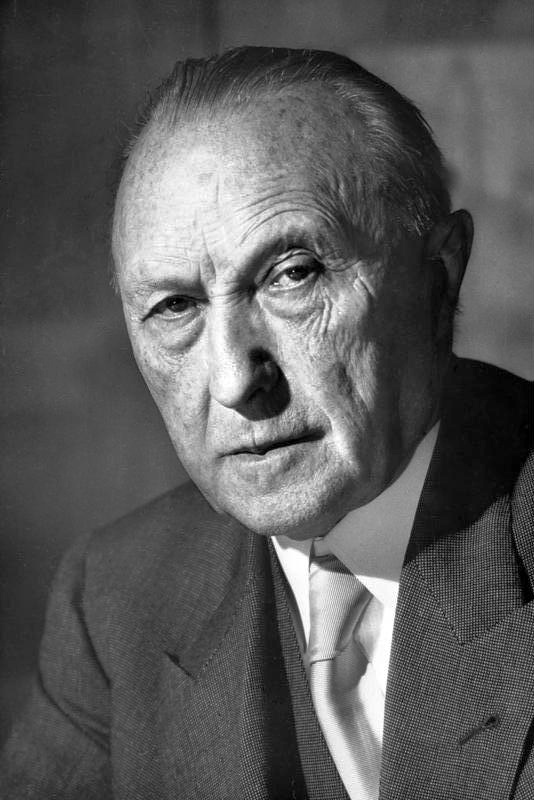 Ein schwarz-weiß-Foto von Konrad Adenauer in Anzug und Krawatte. Er hat eine große Halbglatze und einige verbleibende Haare über die Glatze frisiert.