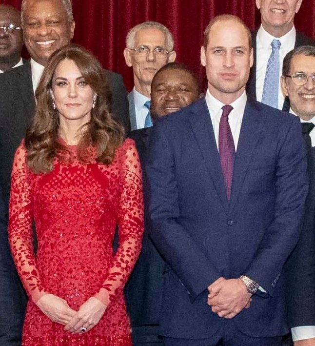 Prinz William und Herzogin Catherine in festlicher Kleidung auf einem Gruppenbild. Sie trägt ein Spitzenkleid, er Anzug und Krawatte.
