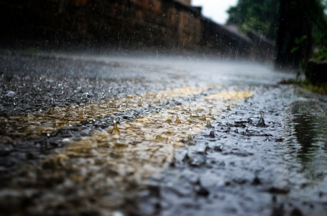 Regentropfen werden vom Wind verweht und fallen auf eine Straße mit gelben Markierungen.