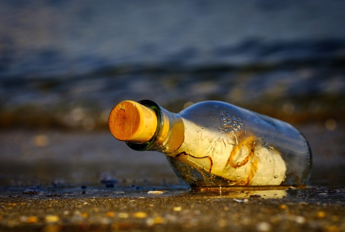 Eine verkorkte Flasche mit einem Brief im Inneren liegt am Strand.
