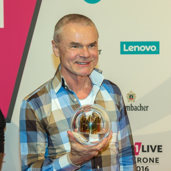 Jürgen Domian in einem karierten Hemd und kurzen grauen Haaren. Er hält eine Preisstatue der 1 Live Krone in der Hand.
