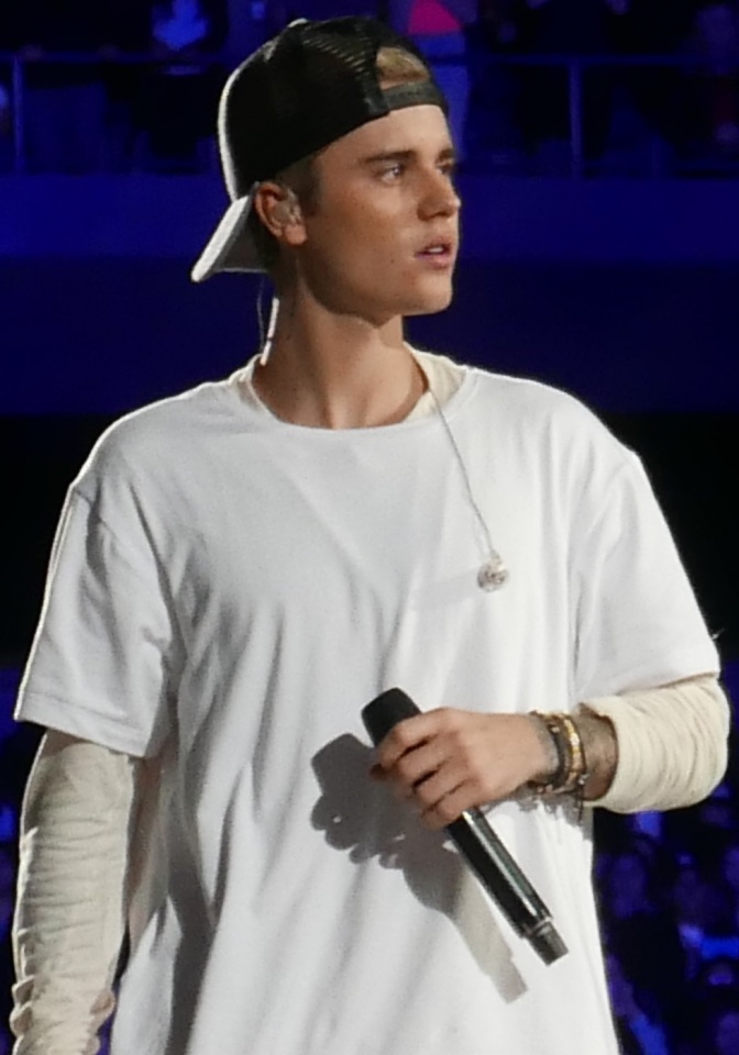 Justin Bieber in einem weiten T-Shit und mit nach hinten gedrehter Baseballmütze. Er hält ein Mikrophon in der Hand.