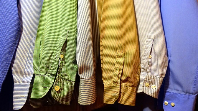 Mehrere verschiedenfarbige Hemden, zum Teil mit Muster, hängen nebeneinander auf Bügeln.