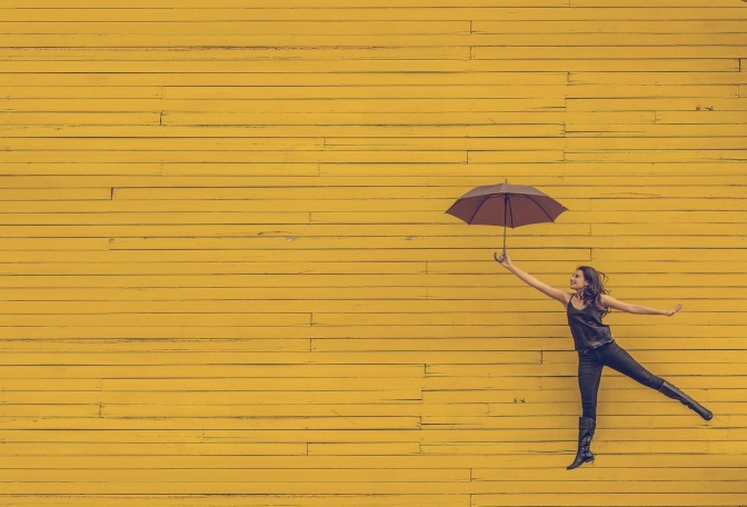 Eine Frau hält einen aufgeklappten Regenschirm in der Hand und springt in die Luft.