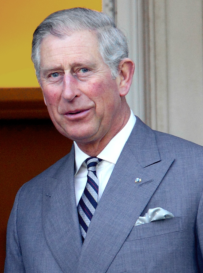 Prinz Charles mit Stirnglatze und nach hinten frisierten Haaren. Er trägt Anzug und Krawatte und ein Einstecktuch.