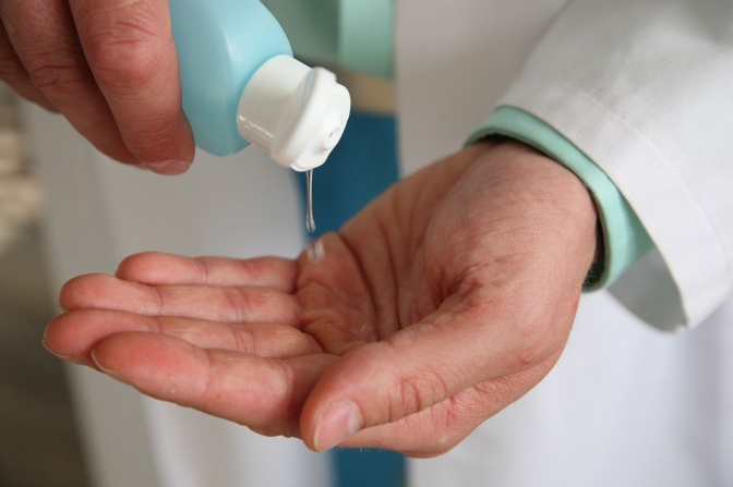 Eine Person im Arztkittel schüttet sich aus einer Plastikflasche eine klare Flüssigkeit in die Hände.
