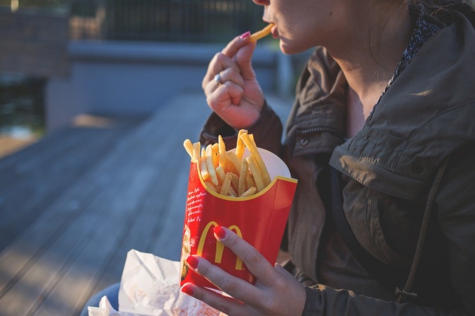 Eine Frau sitzt im Freien und isst Pommes aus einer Packung mit McDonalds-Logo.