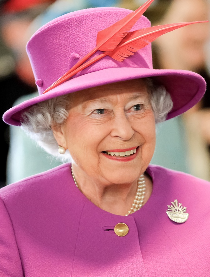 Queen Elizabeth in Hut und Kostüm, mit weißen Haaren und Brosche.