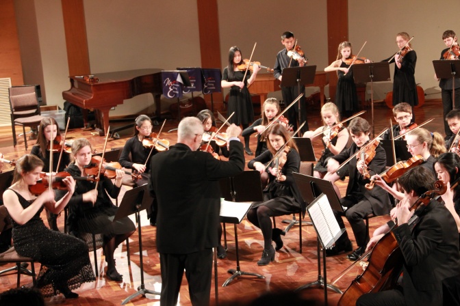 Klassische Musiker und Musikerinnen eines Orchesters spielen zusammen, dirigiert von einem Dirigenten.