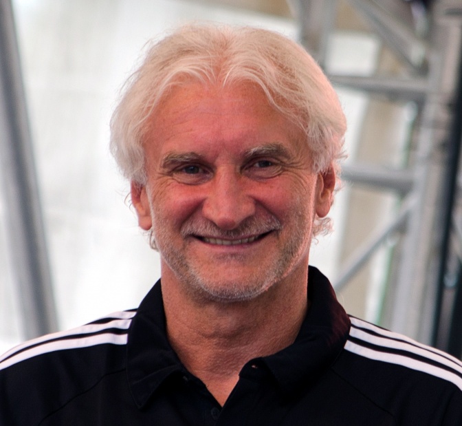 Rudi Völler mit gewellten, weißen Haaren in einer Trainngsjacke mit 3 Streifen auf der Schulter.