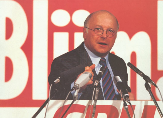 Norbert Blüm vor einem Wahlplakat mit seinem Namen. Vor ihm viele Mikrophone.