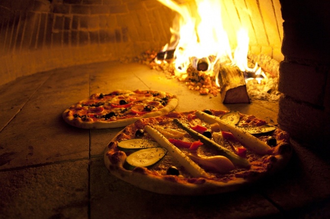 Zwei Pizzen in einem Holzofen mit offenem Feuer