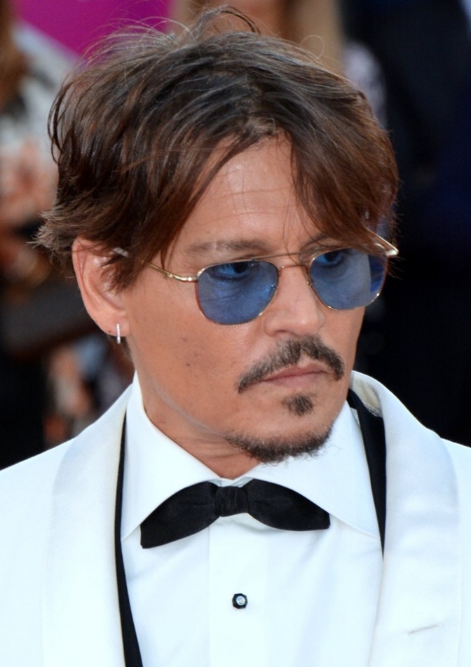 Johnny Depp mit getönter runder Brille in Anzug und Fliege.