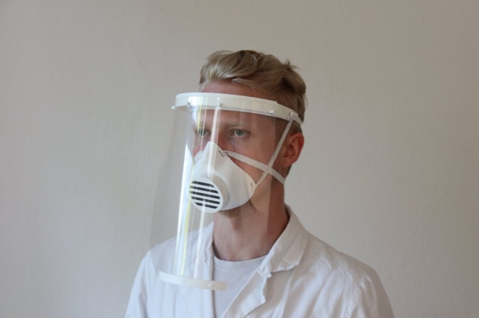 Ein Mann in einem weißen Kittel mit einem durchsichtigen Schutzschild vor dem Gesicht