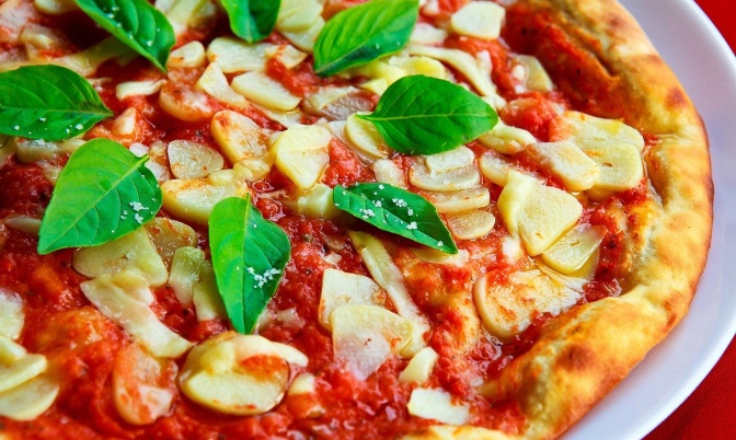 Eine Pizza, belegt mit Tomate, Käse, viel Knoblauch und frischem Basilikum
