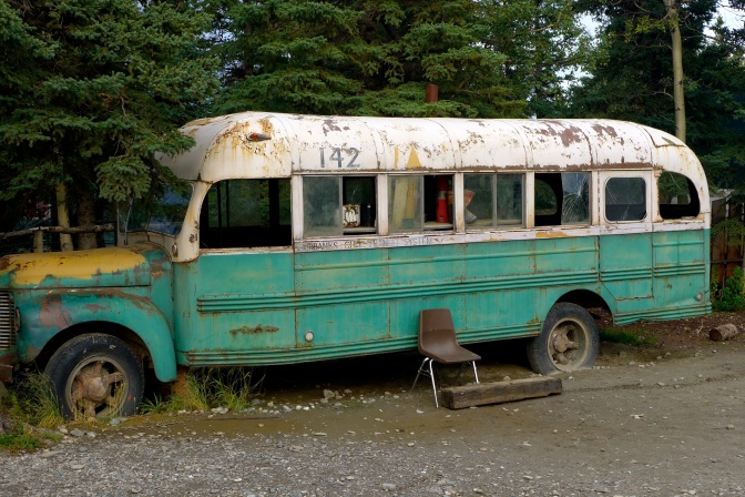 Ein alter Bus, der rostend vor einer Baumreihe steht.