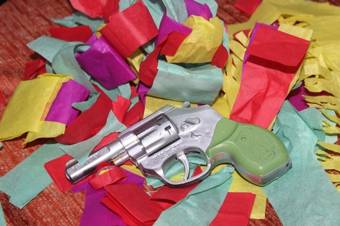 Eine Spielzeugpoistole aus Plastik liegt auf farbigem Papierkonfetti.